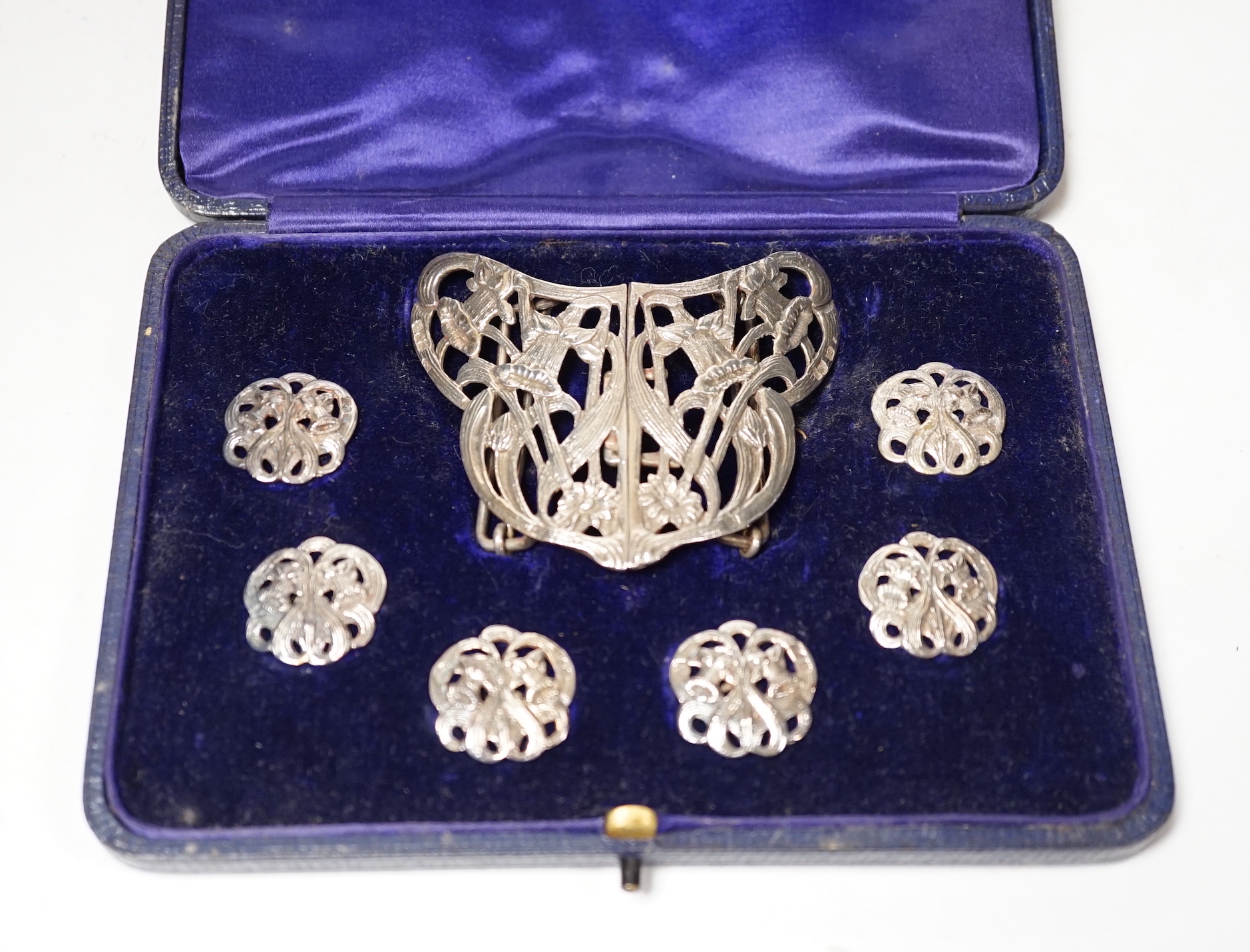 An Edwardian cased silver buckle and button set comprising a buckle and six buttons, Samuel Jacob, London, 1908, buckle width 76mm.